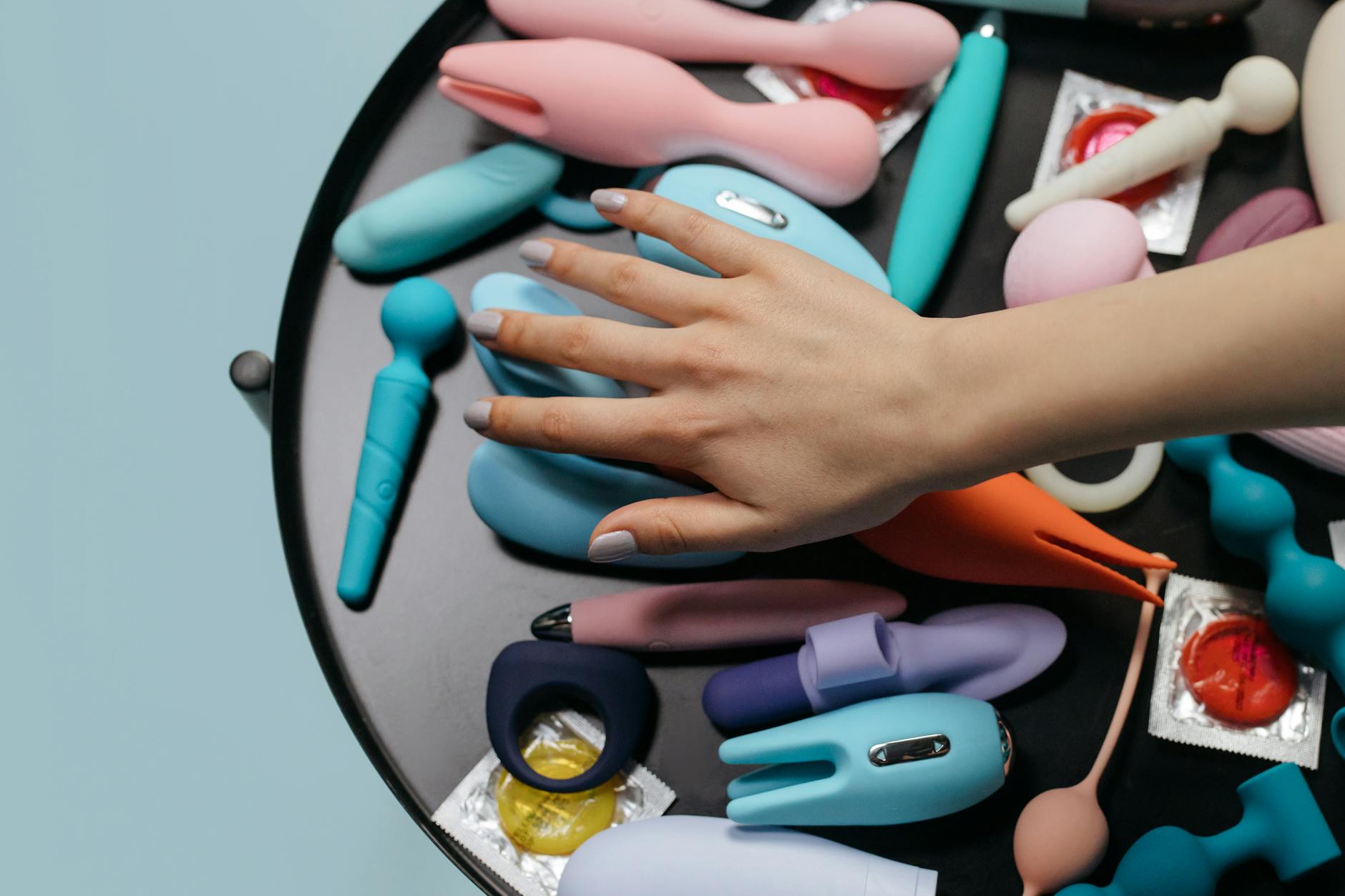 Woman holding blue and pink silicone vibrators in a thoughtful moment