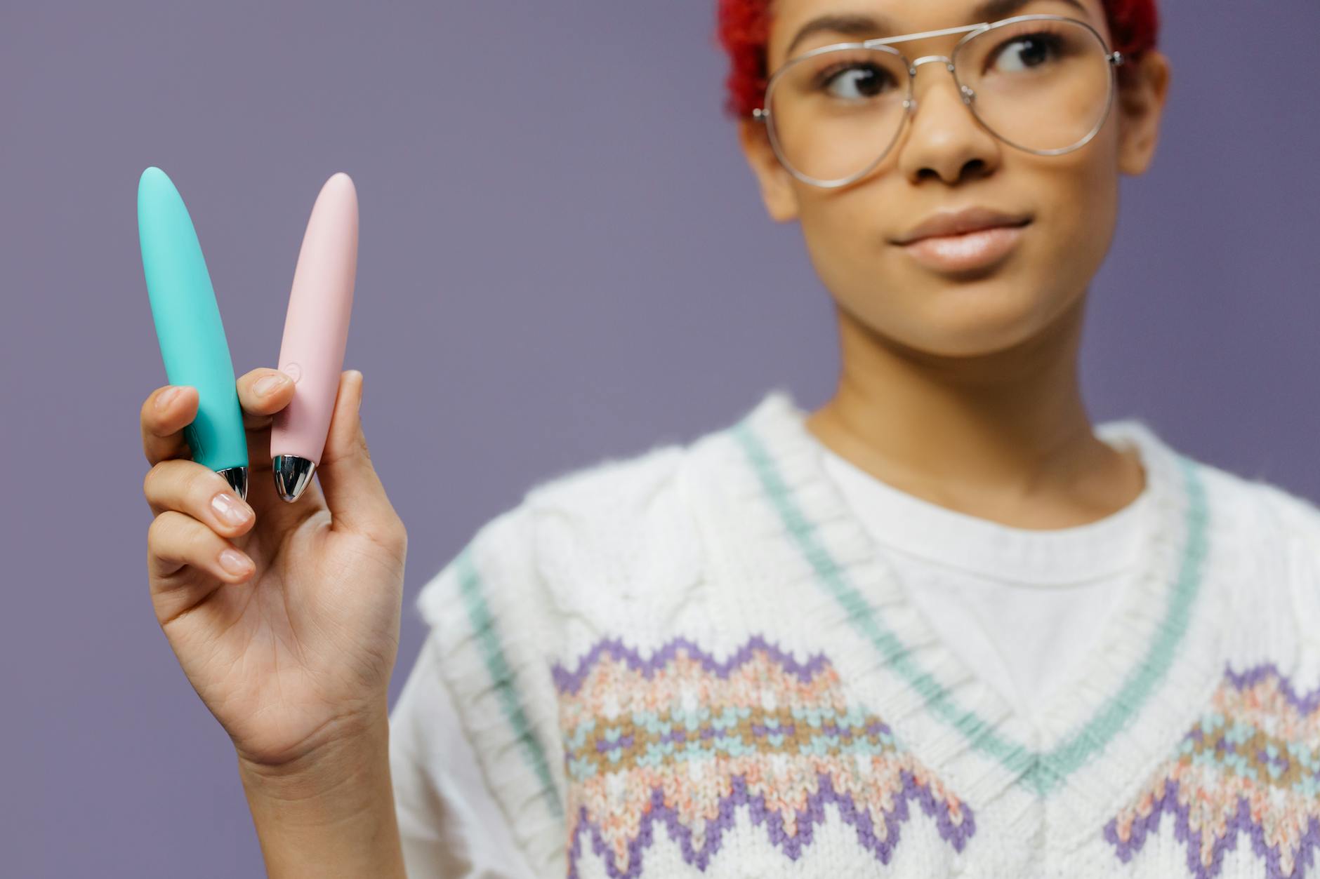 A woman holding two colorful vibrators against a purple background, representing choice and variety for different preferences.