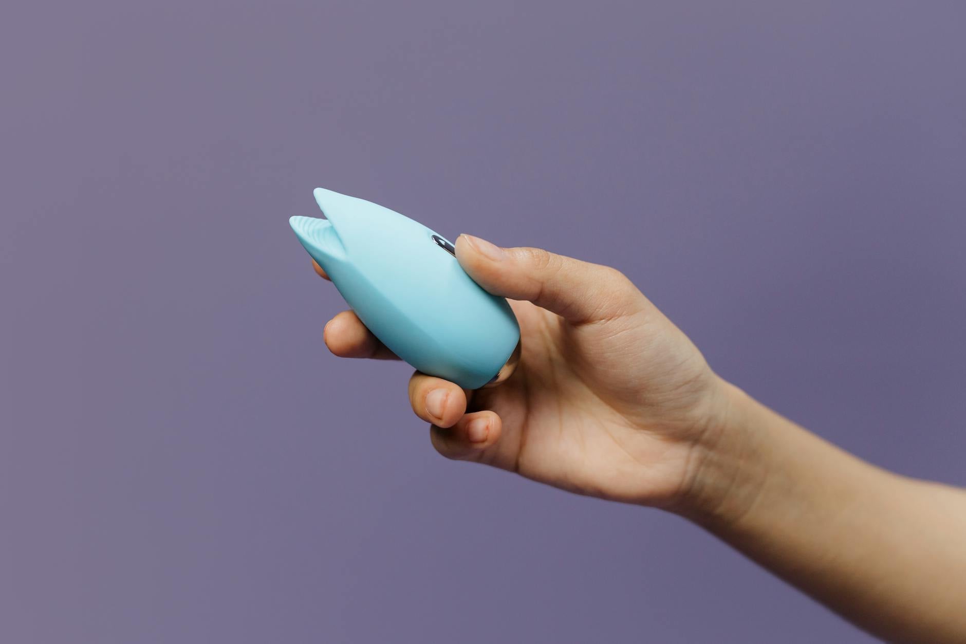 A blue silicone clitoral vibrator held gently in hand, representing reconnection with pleasure