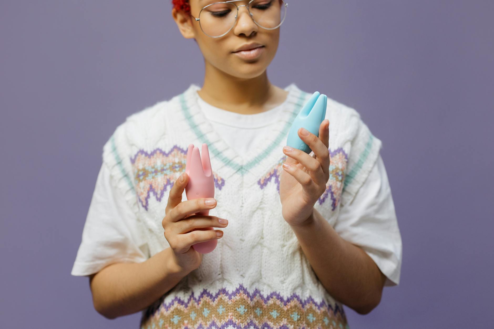 Two hands holding colorful clitoral vibrators in a moment of shared choice and intimacy