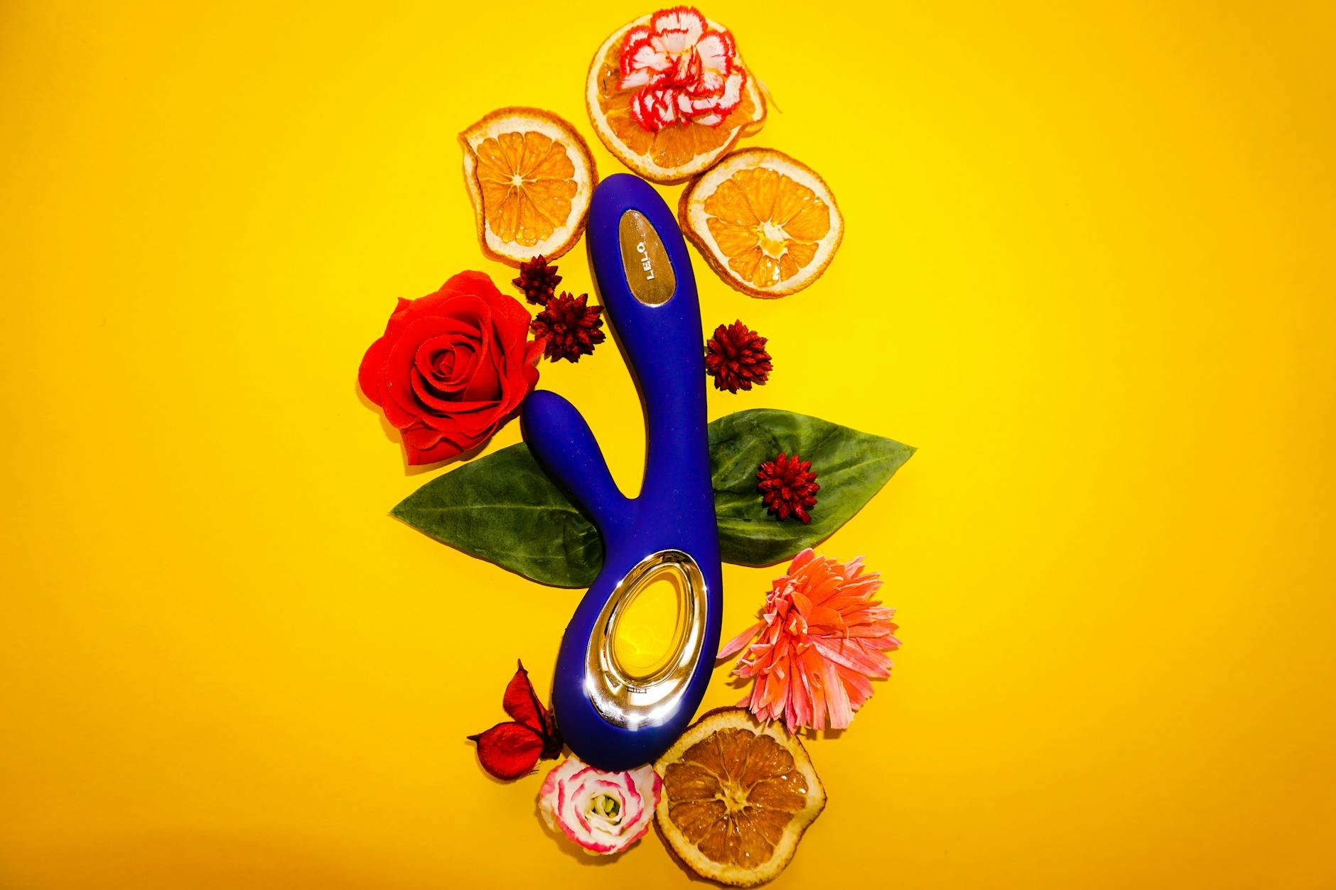 A blue lemon vibrator surrounded by flowers and citrus on a bright yellow background.